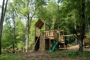 A wooden play structure in a forested area with a slide.