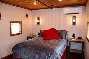 A bedroom with a bed, bedside tables, a window, an air conditioner, and wall-mounted lights.