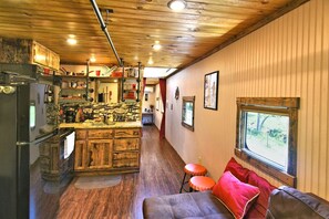 A kitchen with a wooden countertop, a refrigerator, and a dining area with a couch and stools. - Glamping Caboose Rental Perfect for Families near Clyde, North Carolina (Clyde)