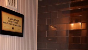 A bathroom with a toilet, a trash can, and a sign on the wall.