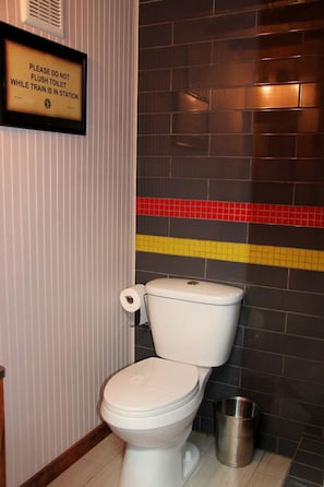 A bathroom with a toilet, a trash can, and a sign on the wall.