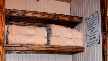 A bathroom with wooden shelves holding towels, a sign with toilet rules, and a clock on the wall.