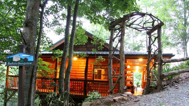 Una cabaña de troncos con porche, rodeada de árboles, y un letrero que indica que es el 'Buffalo Bungalow'.