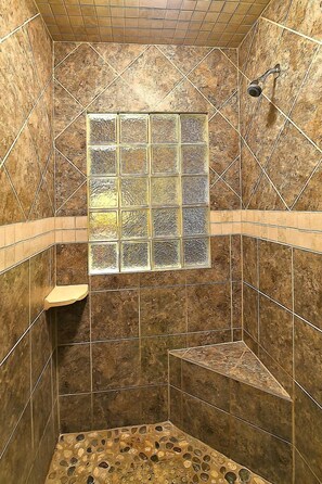 Ducha con pared de azulejos, ventana y cabezal de ducha.