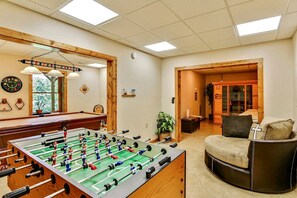 A room with a foosball table, a billiards table, and a comfortable seating area with a sofa and armchairs.