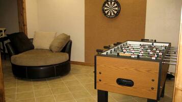 A room with a foosball table, a dartboard, and a round couch.