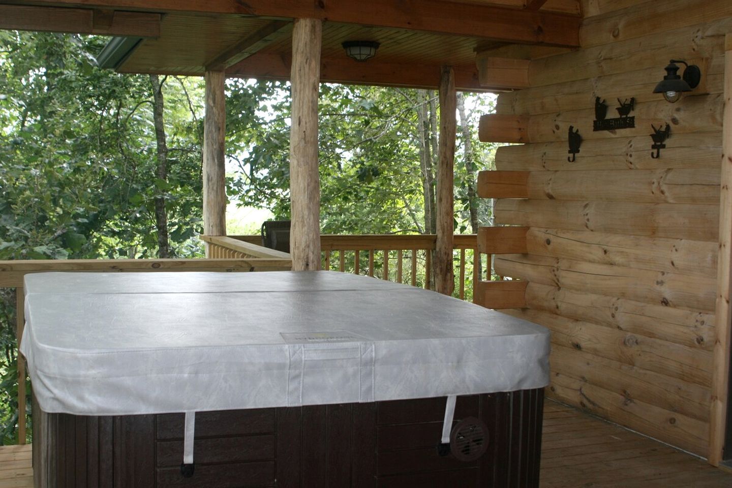 A covered outdoor hot tub area with a wooden deck and a view of trees.