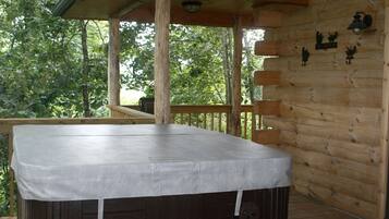 A covered outdoor hot tub area with a wooden deck and a view of trees.