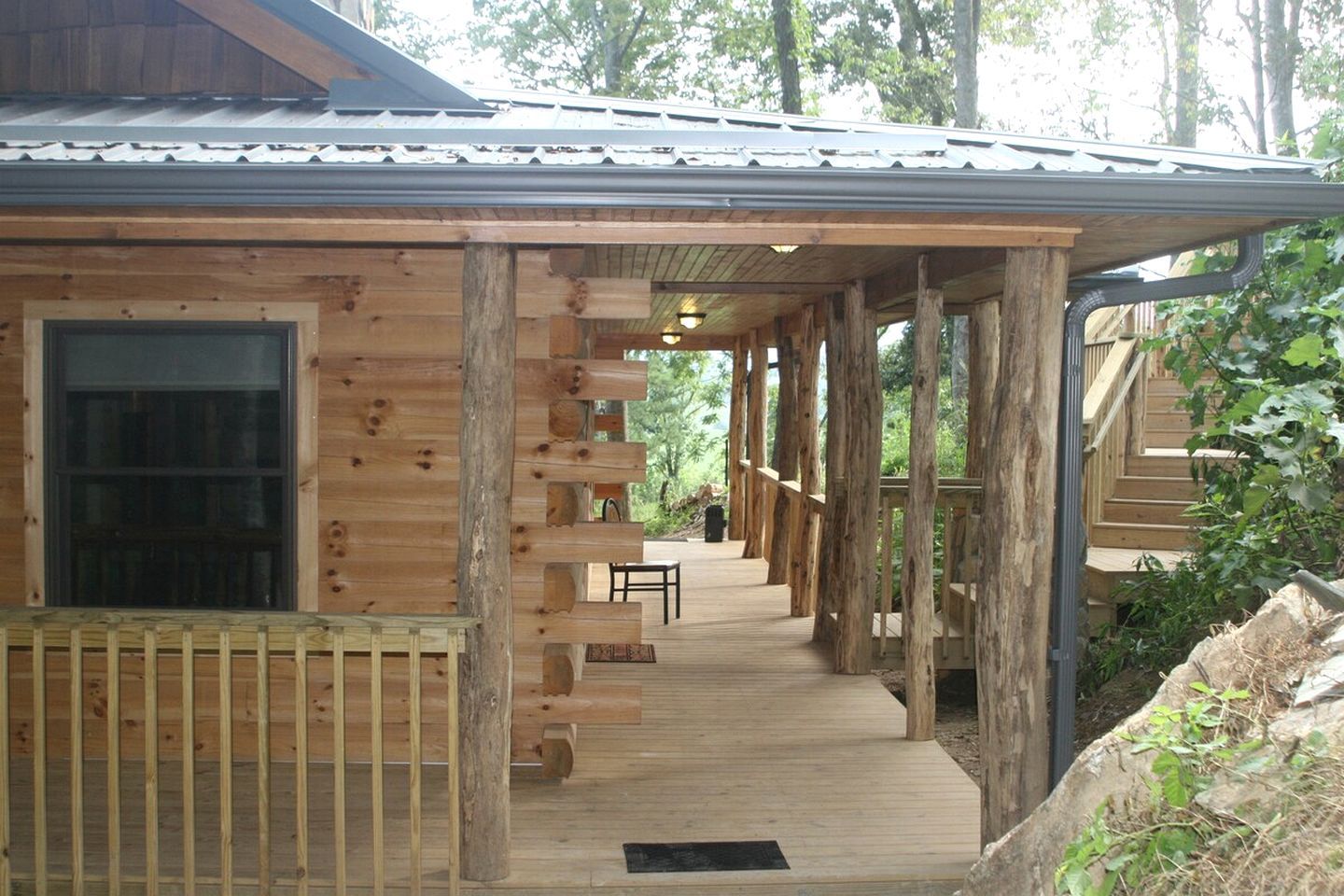 Une cabane en bois dotée d’un porche couvert, d’une fenêtre et d’un escalier menant à un étage supérieur.