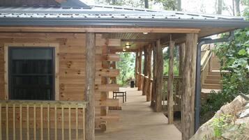 Une cabane en bois dotée d’un porche couvert, d’une fenêtre et d’un escalier menant à un étage supérieur.