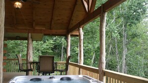 Una terraza de madera con un jacuzzi, sillas y una mesa.