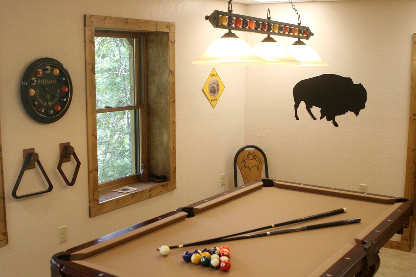 Une table de billard avec des billes, une horloge et un autocollant représentant un buffle sur le mur.