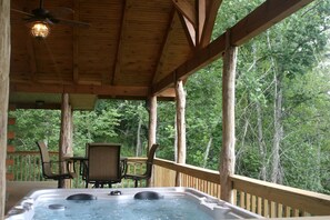 Una terraza de madera con un jacuzzi, sillas y una mesa.