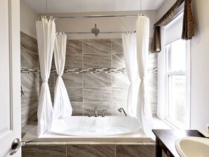 A bathroom with a freestanding bathtub, a shower curtain, and a window with curtains.