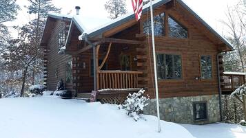 A log cabin with a stone foundation, large windows, and a porch.