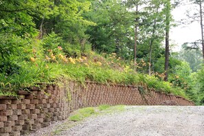Ein Kiesweg neben einer Backsteinmauer, im Hintergrund üppiges Grün und Bäume.