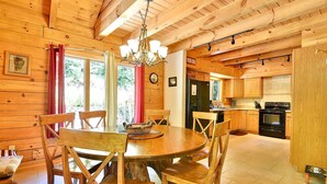 Un interior de madera con una mesa de comedor y sillas, una zona de cocina con armarios de madera y un candelabro.