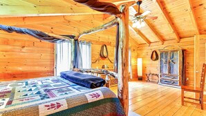 Una habitación de cabaña acogedora, con cama, ventilador de techo e interior de madera rústica.
