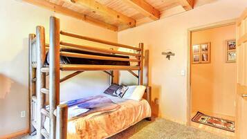 A bunk bed with a ladder, a single bed with a patterned blanket, a door with a mat, and a wall with framed pictures.