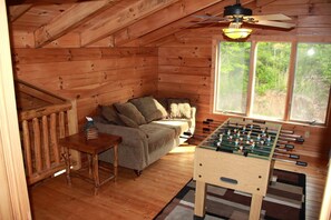 Ein gemütliches Zimmer mit Holzbalkendecke, einer Couch, einem Tisch mit einer Flasche und einem Kicker.