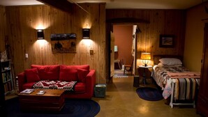Um quarto aconchegante com um sofá vermelho, uma mesinha, uma cama com colcha de patchwork, paredes de madeira e um quadro na parede.
