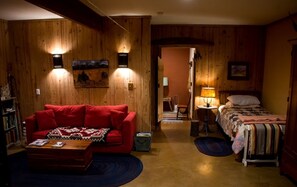 A cozy room with a red sofa, a small table, a bed with a quilt, wooden walls, and a painting on the wall. - Cozy Ground Floor Suite in a Beautiful Farmhouse for a Unique Getaway in Afton, Virginia (Afton)