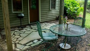 A covered patio with a stone floor, a green metal table and chairs, and a door with a window. - Cozy Ground Floor Suite in a Beautiful Farmhouse for a Unique Getaway in Afton, Virginia (Afton)
