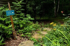 Un jardín con un cartel que indica una Earth Room, rodeado de diversas plantas y un camino de piedra.