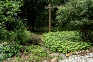 A garden with a wooden cross, dense foliage, and a gravel path.