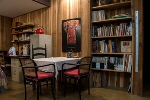 Una habitación con pared de madera, una estantería, una mesa con sillas y un cartel.
