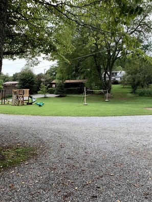A residential area with a grassy lawn, a swing set, and a small play structure. - Cozy Creekside Cabin Rental in Bryson City, North Carolina (Bryson City)