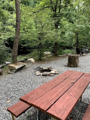 A picnic area with a wooden bench, a fire pit, and a stone bench.