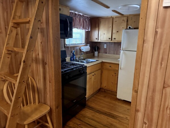 Une cuisine de taille réduite, dotée de meubles de rangement en bois, d’une cuisinière, d’un évier et d’un réfrigérateur.