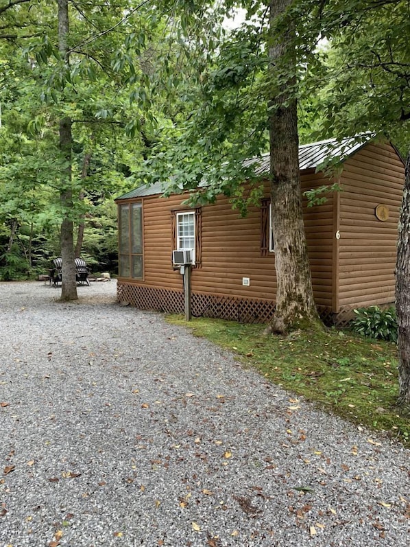 A wooden cabin with a gravel driveway, surrounded by trees.