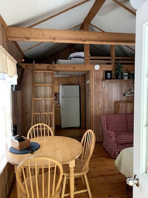 A rustic cabin interior with a wooden dining table, chairs, a refrigerator, and a bunk bed. - Cozy Creekside Cabin Rental in Bryson City, North Carolina (Bryson City)