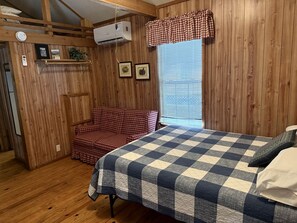 Una habitación con paredes de madera, una cama con colcha a cuadros, una silla roja a cuadros y una ventana con persianas.