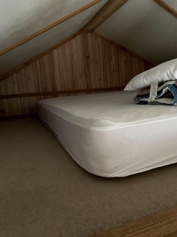An attic bedroom with a mattress, wooden walls, and a sloped ceiling.