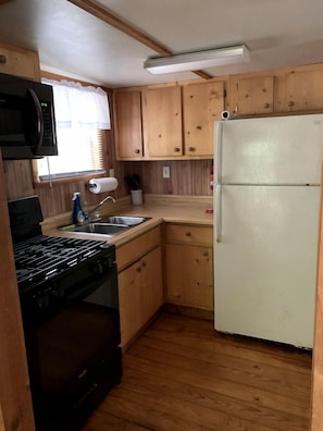 A compact kitchen with wooden cabinets, a stove, a microwave, a sink, and a refrigerator.