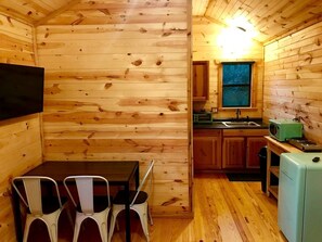 Una cabaña de madera compacta con comedor, cocina y un refrigerador pequeño.