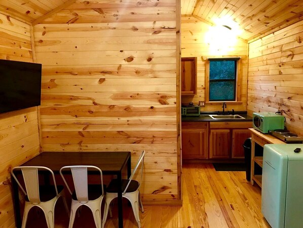 Una cabaña de madera compacta con comedor, cocina y un refrigerador pequeño.