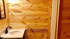 Ein kleines Badezimmer aus Holz mit Waschbecken, Spiegel, Handtuchhalter und einer kleinen Fußmatte.