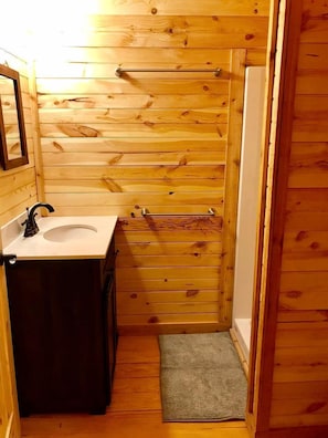 Ein kleines Badezimmer aus Holz mit Waschbecken, Spiegel, Handtuchhalter und einer kleinen Fußmatte.