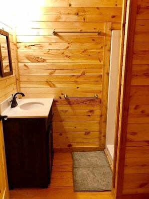 Une petite salle de bain en bois, avec un lavabo, un miroir, un porte-serviettes et un petit tapis.