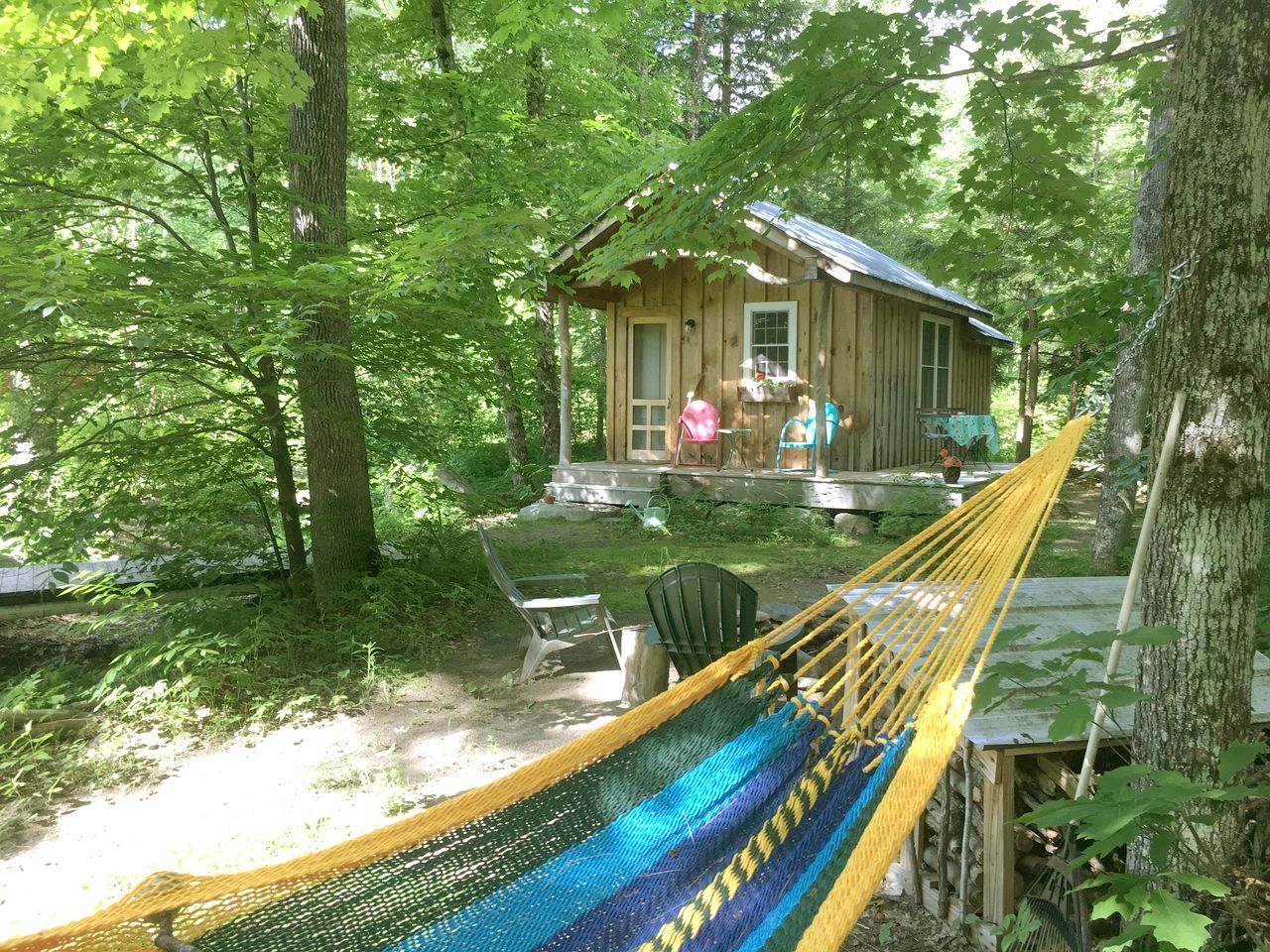 Une cabane en bois avec un porche, entourée d’arbres. On y trouve un hamac et du mobilier d’extérieur.