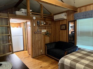 A compact room with a bed, a sofa, a kitchen area, and a wooden ceiling.