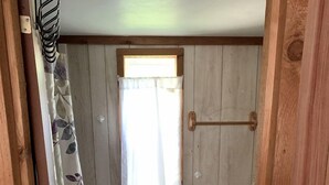 Un baño pequeño con inodoro, una ventana con cortina y suelo de madera.