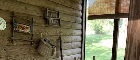 Interior de cabaña con paredes de madera, una mecedora, una mesa y un ventanal con vistas a la vegetación.