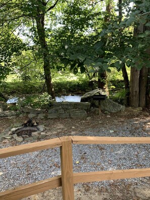 A natural outdoor setting with a wooden fence, a small stream, and a stone fire pit.