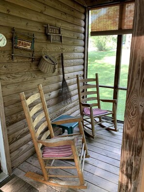 Ein Urlaubsdomizil mit Holzwänden, einem Schaukelstuhl, einem Tisch und einem Fenster mit Blick auf Grün.