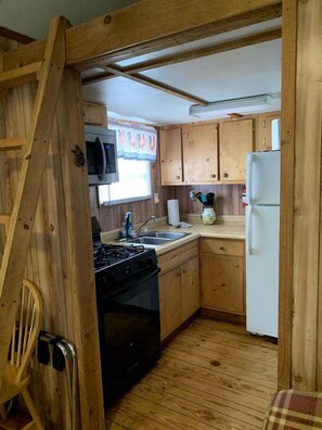 Eine kleine Küche mit Holzschränken, einem Herd, einem Spülbecken und einem Kühlschrank.